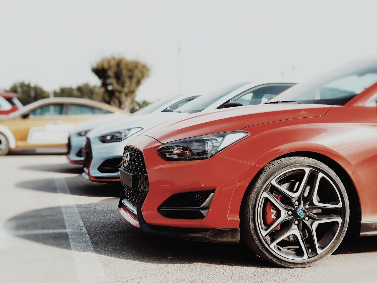 A row of colorful cars parked outdoors in a sunny car park, highlighting the vehicles' design.